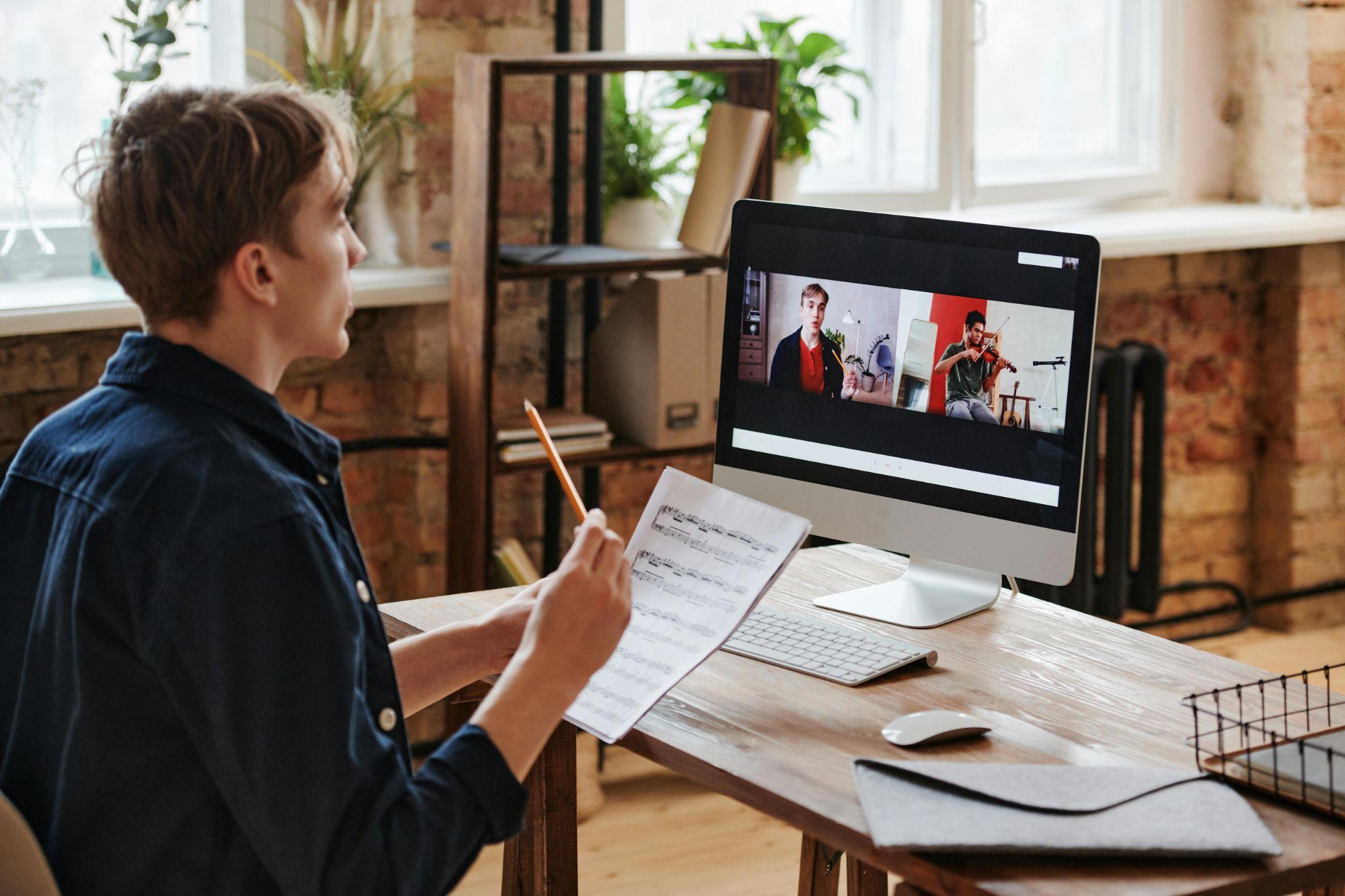 A young musician is attending an online music lesson on a desktop computer